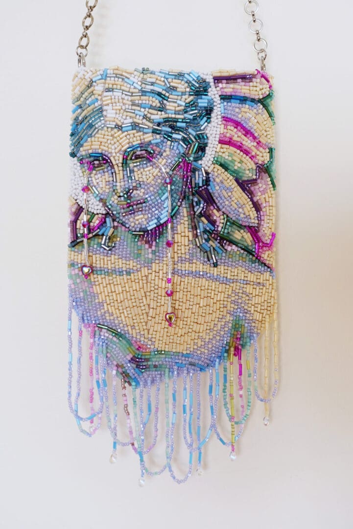 Beaded handbag featuring a detailed, colorful portrait of a Angel with flowing hair and fringe details hanging from the bottom.